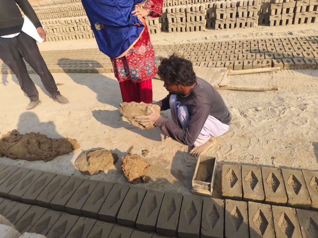 A person molding wet clay into bricks by hand at a brick kiln in Pakistan.